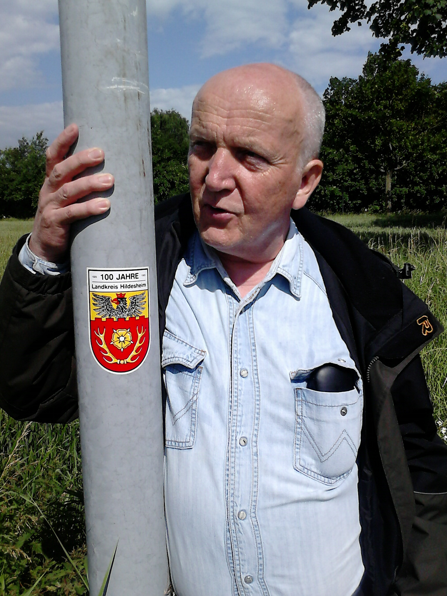 Farbfoto: Erwin Thomasius auf der Wanderung vom Bahnhof Nordstemmen zur Marienburg am Sonntag, dem 15. Juni im Jahre 2014 vor einem Pfahl mit dem Aufkleber HUNDERT JAHRE Landkreis Hildesheim 1885 - 1985. Fotograf: R.I.