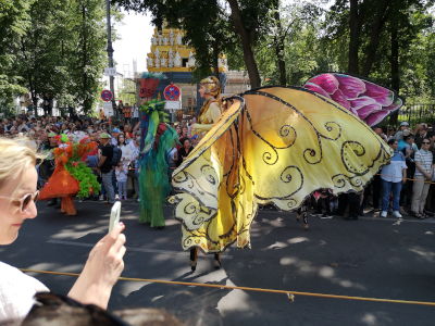 Farbfoto von als Schmetterling verkleideter Stelzenläuferin auf dem Umzug vom Karneval der Kulturen auf der Straße Hasenheide in Berlin am 28. Mai 2023. Fotograf: Erwin Thomasius.