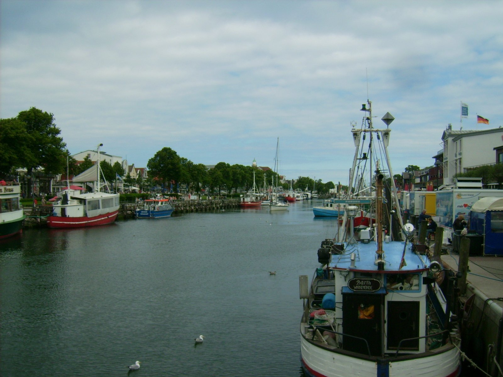 Farbphoto: Schiffe und der Verkauf von frischem Fisch in Buden auf dem Ufer in Warnemünde im Juni 2009. Photograph: Bernd Paepcke.